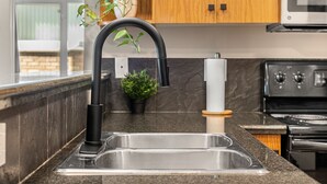 Eine Küche mit Spüle aus Edelstahl, einem schwarzen Wasserhahn, einer Mikrowelle über dem Herd und Holzschränken.