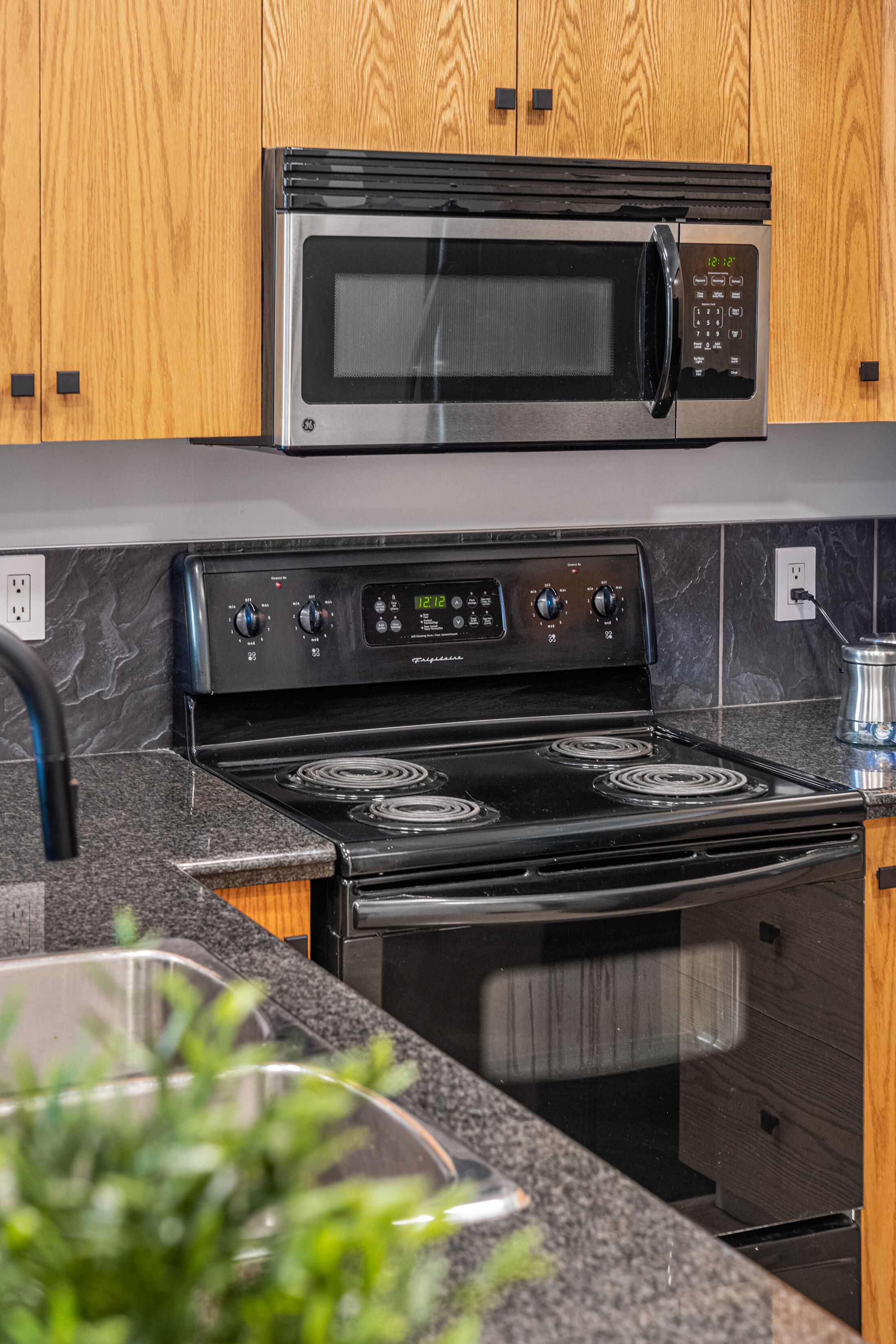 Une cuisine équipée d’un four à micro-ondes en acier inoxydable, d’une cuisinière noire et de meubles de rangement en bois.