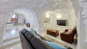 Tunnelmallinen olohuone, jossa on kiviseinä, nahkasohva, puinen sohvapöytä, ruskea nojatuoli ja televisio.