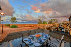 An outdoor dining area with a table set for six, surrounded by chairs, with a stone wall and a view of the landscape.