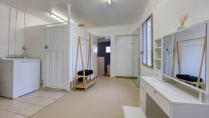Huoneessa on valkoinen vaatekaappi, peili, puinen tikapuu ja pesukone.