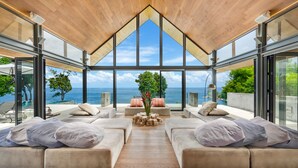 A modern interior with a wooden ceiling, large glass windows, and a seating area with cushions. - Villa Saengootsa (Kamala)