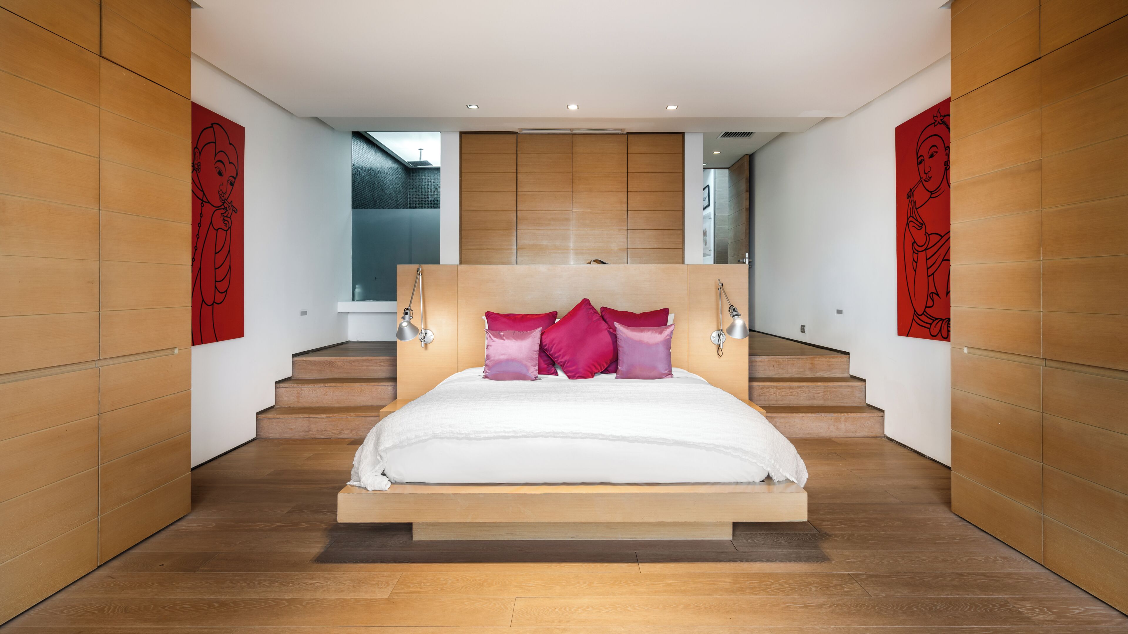 A modern bedroom with a wooden headboard, a large bed with white bedding, and red accent pillows.