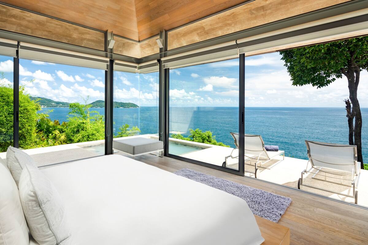 A modern bedroom with a large bed, a view of the sea, and a balcony with seating.