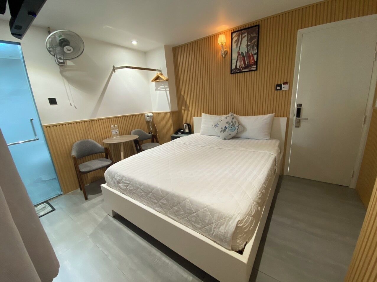 Una habitación de hotel con cama, una silla, una mesita, un ventilador y una puerta.