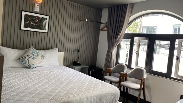 A hotel room with a bed, two chairs, a desk, a lamp, and a window with curtains. - Đông Như 3 (Ho Chi Minh City)