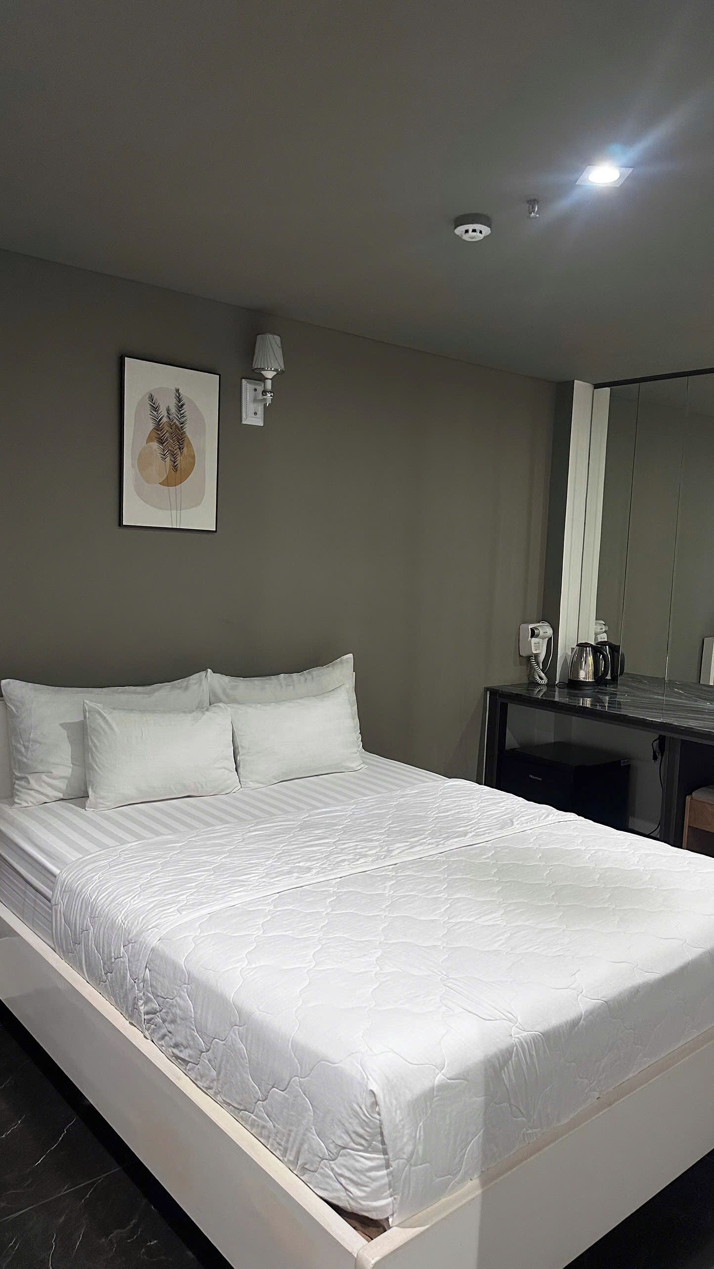Een hotelkamer met een bed, een bureau, een lamp en een ingelijst schilderij aan de muur.