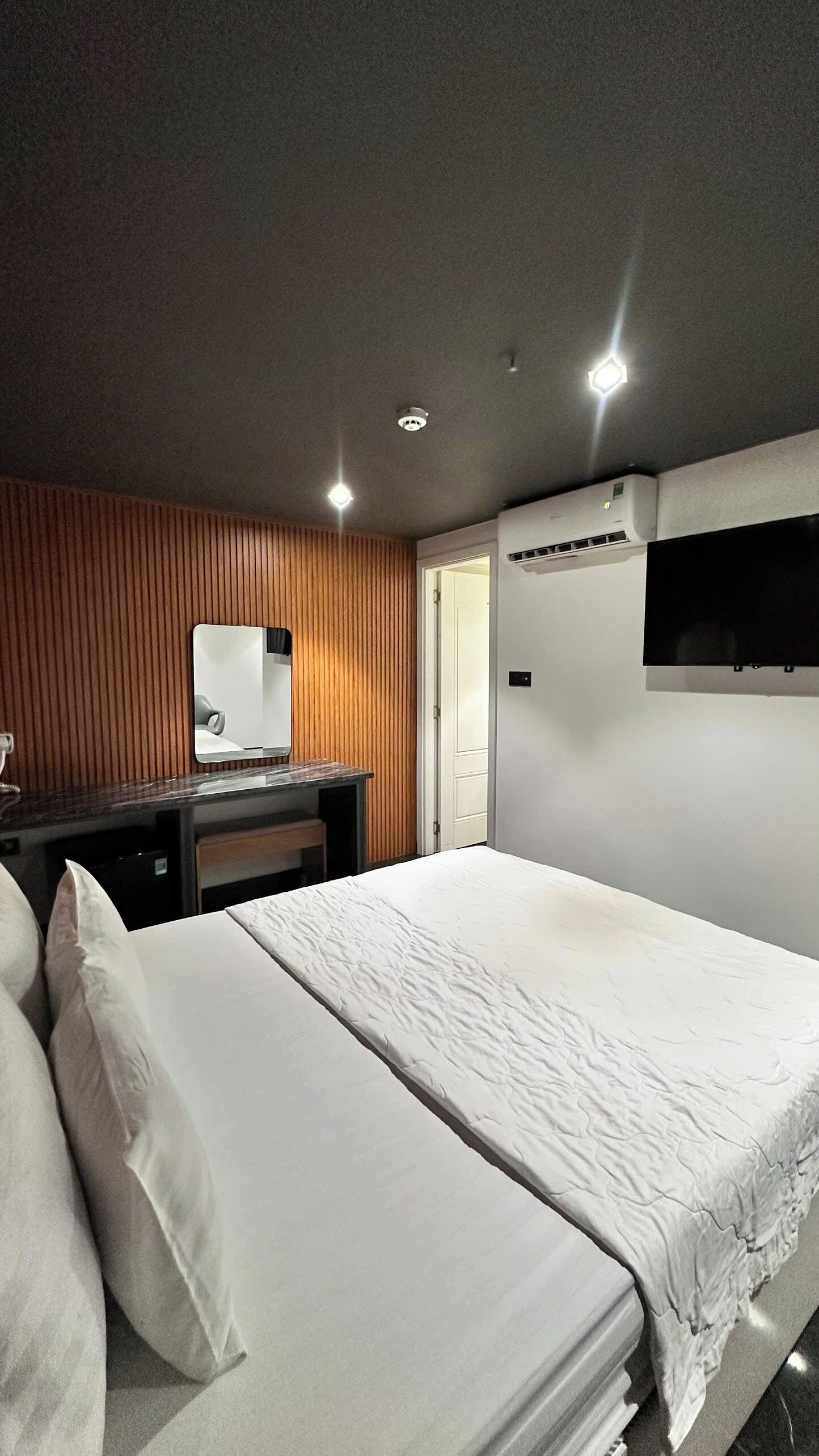 A hotel room with a bed, a desk, a mirror, and a TV mounted on the wall.