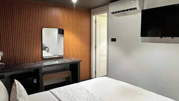 A hotel room with a bed, a desk, a mirror, and a TV mounted on the wall.