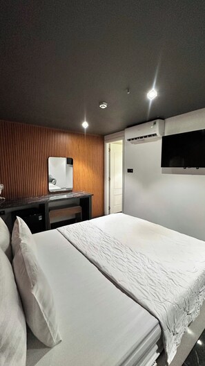 Een hotelkamer met een bed, een bureau, een spiegel en een aan de muur bevestigde televisie.