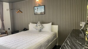 A hotel room with a bed, a bedside table, a desk, a chair, a hanging light, and a wall-mounted TV. - Đông Như 3 (Ho Chi Minh City)