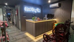 A hotel reception area with a neon sign, a reception desk, and a seating area with a wooden chair. - Đông Như 3 (Ho Chi Minh City)