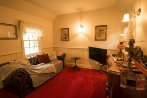 A cozy room with a red carpet, a leather sofa, a television, and a chessboard.