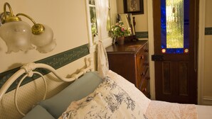 Une chambre à coucher comprenant un lit, une commode, une fenêtre avec des vitraux et un luminaire fixé au mur.