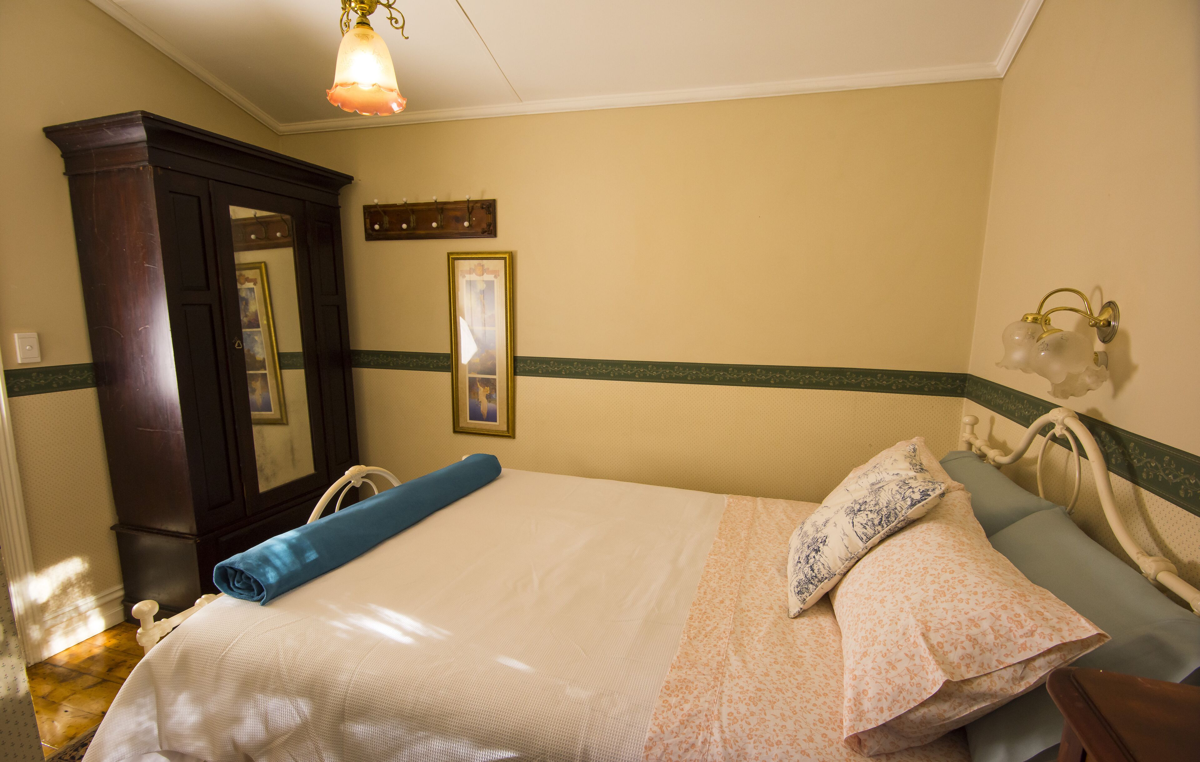A neatly made bed with a blue towel, a floral-patterned pillow, and a mirror above it.