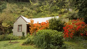 Une petite maison à toit en pente, entourée d’une végétation luxuriante et de plantes en fleurs.