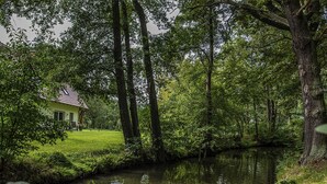 Une maison avec un toit rouge, entourée d’une végétation luxuriante et bordée d’une rivière paisible.