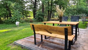 Une terrasse extérieure en bois, avec une table et des chaises, entourée de verdure et d’arbres.