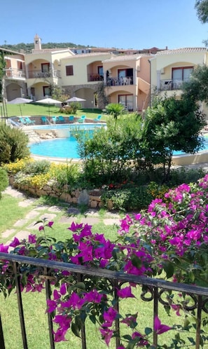 A hotel with a swimming pool, outdoor seating, and a garden with bougainvillea flowers.