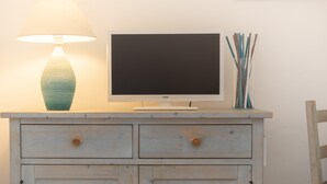 A television on a wooden cabinet with two drawers and a lamp beside it.
