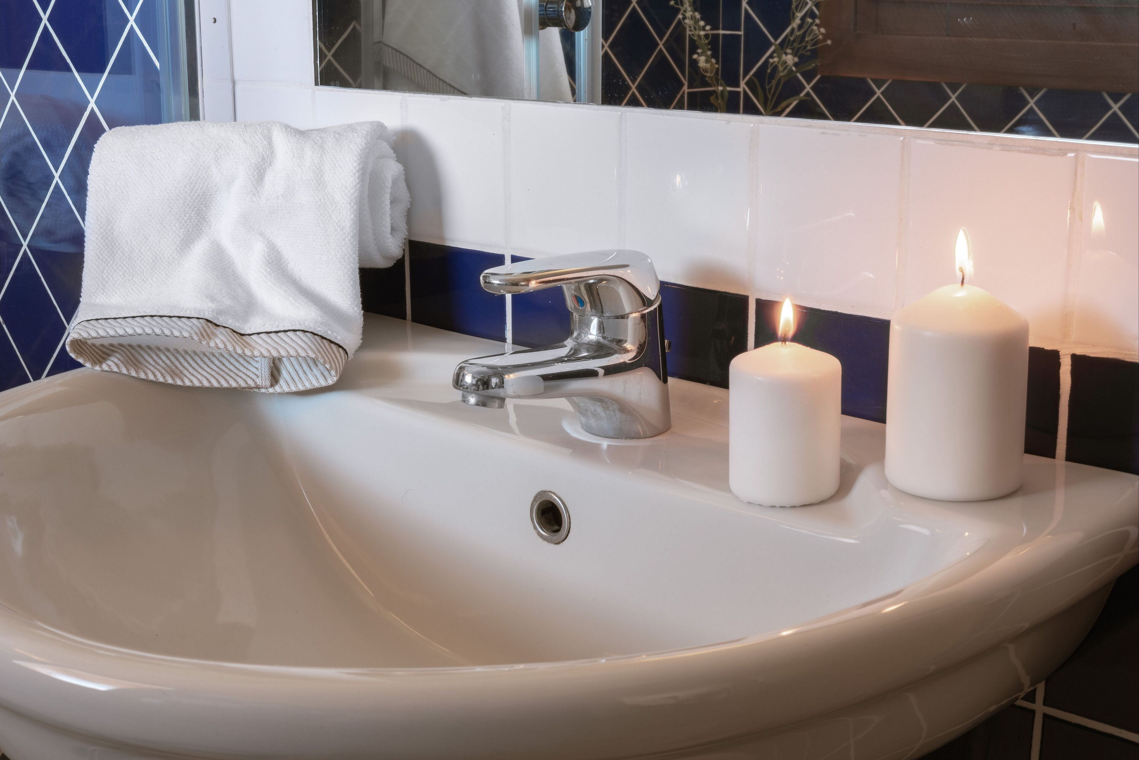 A bathroom sink with a chrome faucet, two lit candles, and a white towel on a rack.