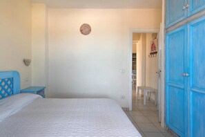 A bedroom with a bed, a nightstand, a wardrobe, and a door leading to a hallway.