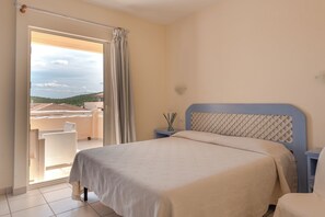 A bedroom with a bed, a nightstand, a window with curtains, and a view of the outside. - Fantastico Baia de Bahas Residence Sea View 2 Bedroom sleeps 6 (Marinella)