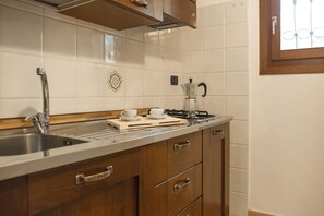 Een keuken met een RVS spoelbak, houten kastjes, een koffiezetapparaat en een raam met een metalen traliewerk.