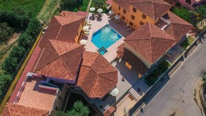 Una propiedad residencial con piscina, varios tejados de tejas rojas y un jardín cuidado.