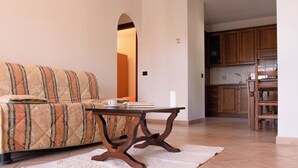 Una sala de estar con sofá, una mesa de centro y una alfombra. Se ve una cocina al fondo.
