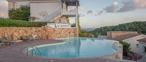 Una piscina con sillas de descanso, un muro de piedra y un edificio con un letrero que dice "Eabinca".