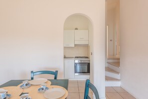 Un comedor con una mesa dispuesta para dos, una cocina con armarios blancos y una estufa a gas, y una escalera que sube a otro piso.