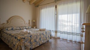 A bedroom with a bed, a nightstand, a lamp, and a window with curtains. - Beautiful Il Giardino degli Oleandri 1 Bedroom sleep 4, plus extra child (Liscia di Vacca)