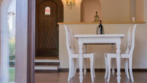 A dining area with a white table and chairs, a wooden door, and a wall-mounted light fixture. - Beautiful Il Giardino degli Oleandri 1 Bedroom sleep 4, plus extra child (Liscia di Vacca)