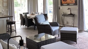 Un salon spacieux avec un plafond haut, des meubles en osier, un coin repas et une vue sur l’extérieur.