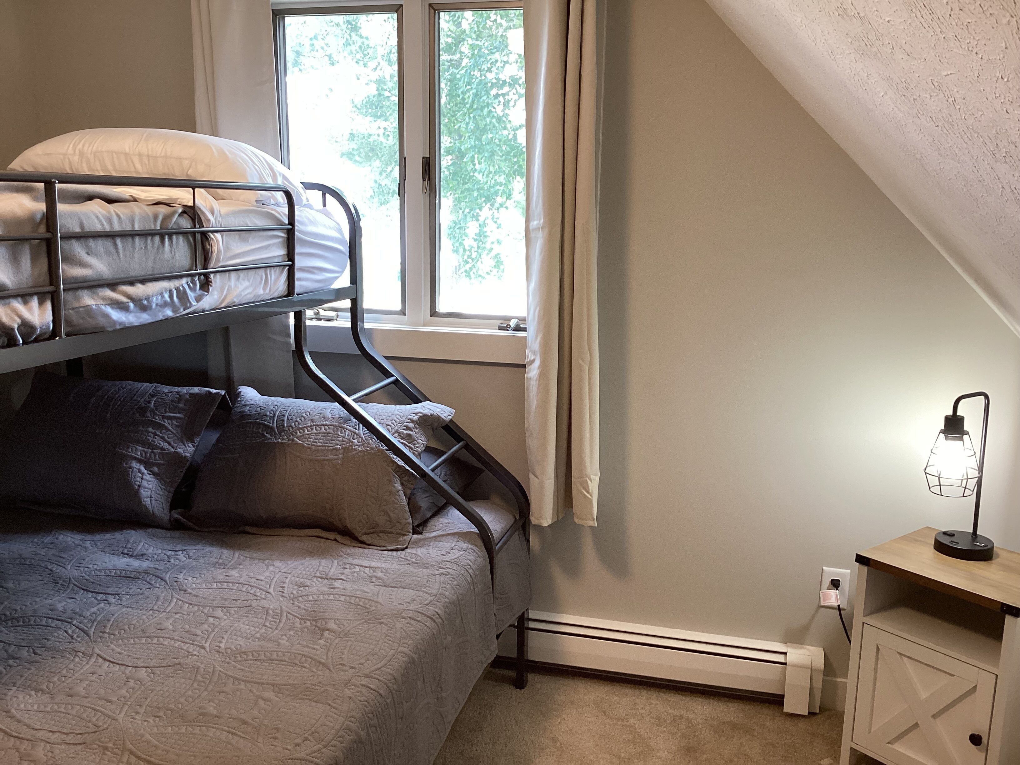 Un lit superposé avec une couvre-lit à motifs, une table de chevet avec une lampe et une fenêtre avec des rideaux.