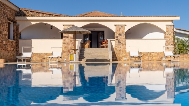 A poolside area with a clear view of a building with stone pillars and a tiled roof.