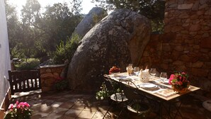 An outdoor dining area with a stone wall, a large rock, and a table set for two with chairs.