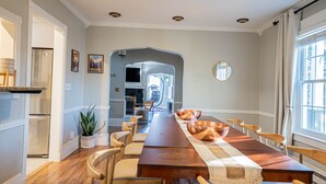 A dining room with a long wooden table, chairs, a potted plant, and a view of the kitchen through an archway. - Modern Antique 5BR Home w/ Expansive Master Suite (Norwich)