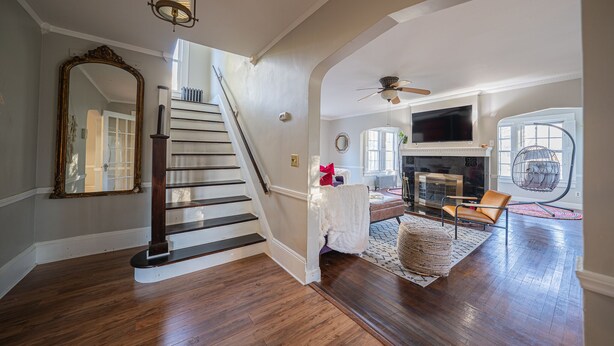 A spacious living area with hardwood flooring, a staircase, a large mirror, a fireplace, and a hanging chair. - Modern Antique 5BR Home w/ Expansive Master Suite (Norwich)