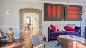 A modern living room with a purple sofa, a coffee table, and a dining area in the background. - Modern Antique 5BR Home w/ Expansive Master Suite (Norwich)