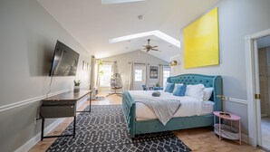 A bedroom with a large bed, a ceiling fan, a TV, and a skylight. - Modern Antique 5BR Home w/ Expansive Master Suite (Norwich)