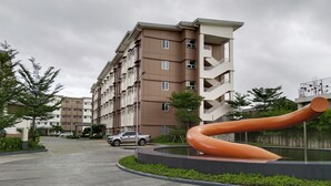 A residential building with multiple floors, balconies, and a curved sculpture in the foreground. - Cozy Unit at SMDC Cheer Residences by Lee Portum (Marilao)