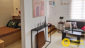 A modern living room with a sofa, a coffee table, and a small table with decorative items. There is a staircase leading to another level. - Cozy Unit at SMDC Cheer Residences by Lee Portum (Marilao)