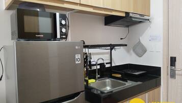 Een kleine keuken met een roestvrijstalen koelkast, een magnetron, een spoelbak en een zwart aanrecht.