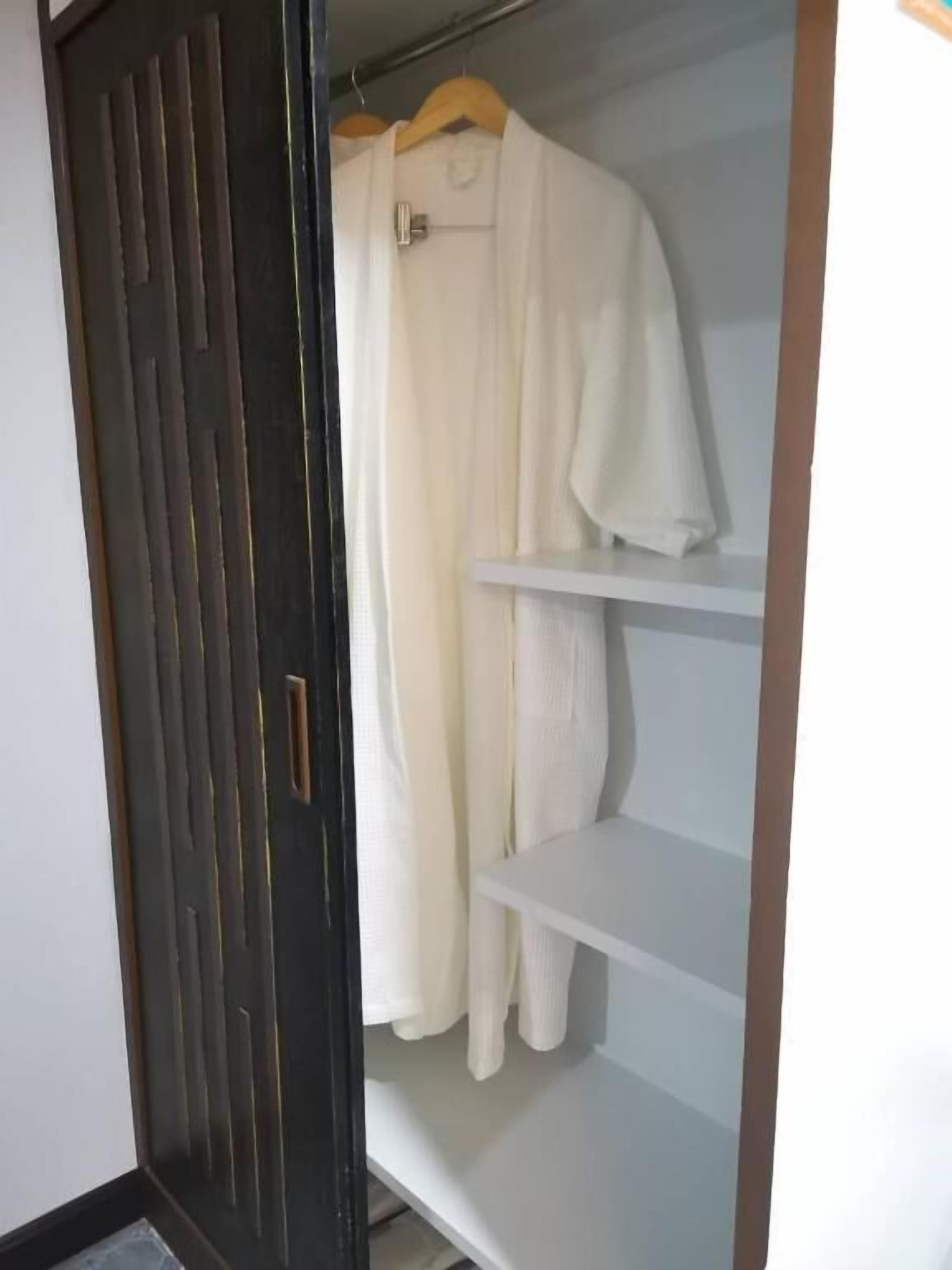 A wardrobe with a dark door and a white robe hanging on a hanger.