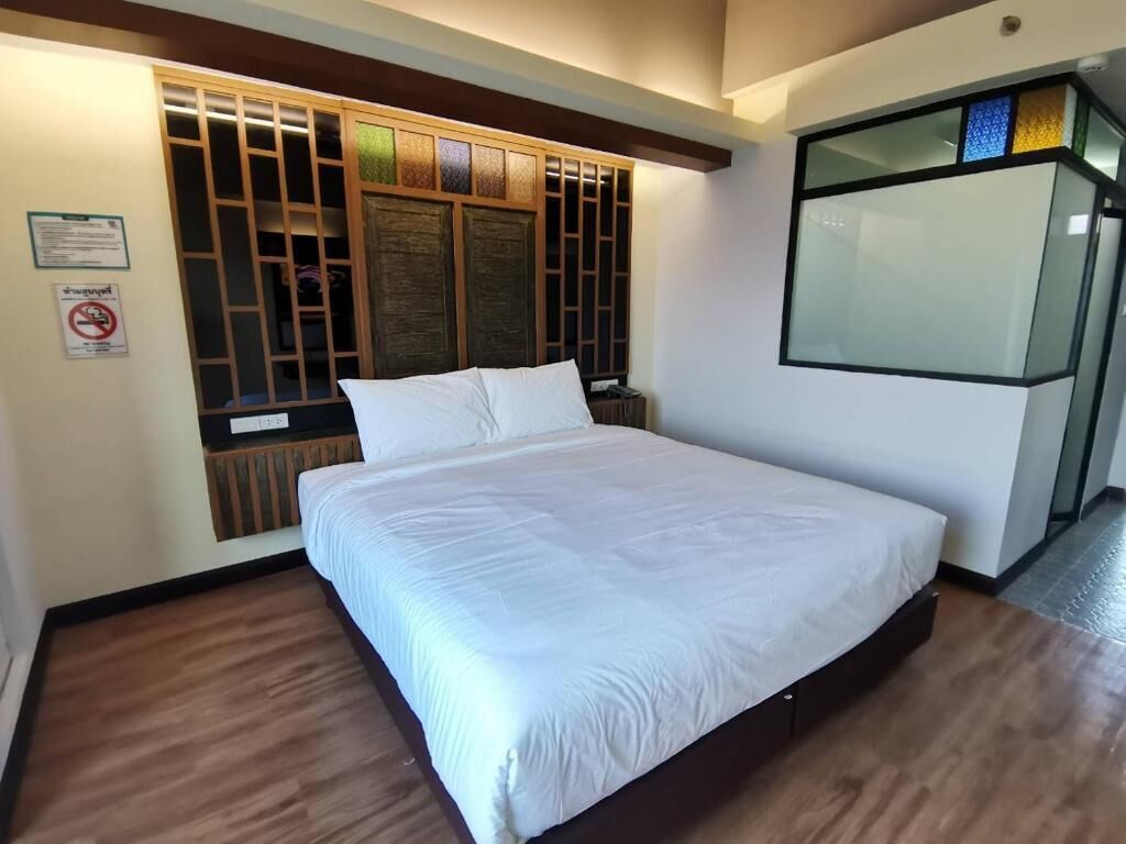 A hotel room with a large bed, a wooden headboard with vertical slats, a glass partition, and a wooden floor.