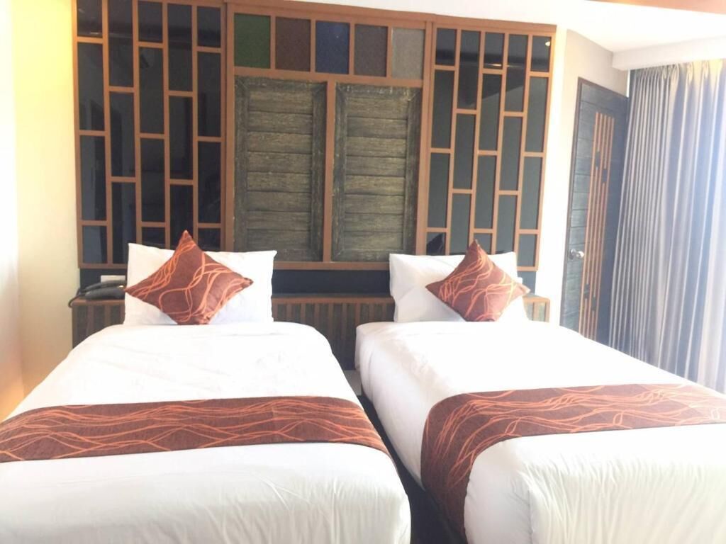 Habitación de hotel con dos camas, cada una con ropa blanca y almohadones marrones estampados. La habitación presenta un panel de madera tradicional con paneles de vidrio y una gran puerta de madera.