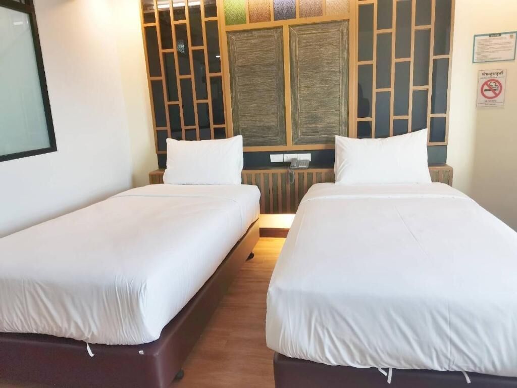 A room with two single beds, a wooden headboard with a decorative panel, a bedside table, and a wall-mounted phone.