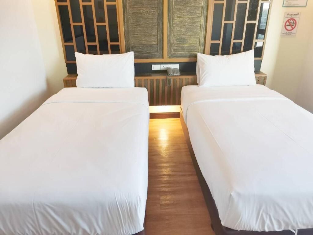 A room with two single beds, wooden headboards, a small bedside table, and a wall-mounted telephone.